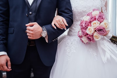新娘拿着粉红色和白色的玫瑰花束而持有武器与她的丈夫。
